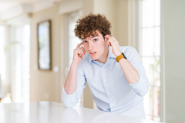 Young business man with curly read head covering ears with fingers with annoyed expression for the noise of loud music. Deaf concept.