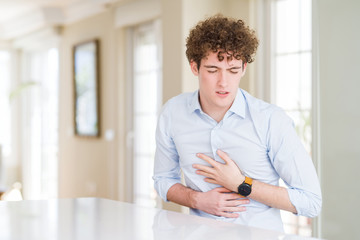 Young business man with curly read head with hand on stomach because indigestion, painful illness feeling unwell. Ache concept.