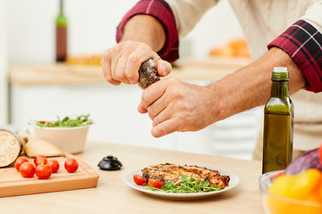 Close up of unrecognizable man sprinkling spices over meat steak while cooking in kitchen, copy space