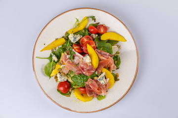 mix salad with ham, blue cheese, tomato, sunflower seeds and mango on white plate.