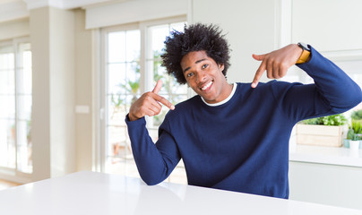 Young african american man wearing casual sweater sitting at home looking confident with smile on...