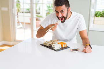 Handsome man smiling happy enjoying eating fresh colorful asian sushi using chopsticks