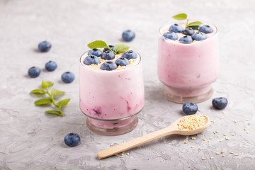 Yoghurt with blueberry and sesame in a glass and wooden spoon on gray concrete background. side view.