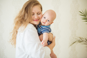 Cute infant baby on mothers hands standing in the room. Mother hugging baby with love. Happy motherhood and maternity concept