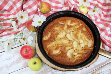Pie with Apple on the wooden white background with a red tablecloth and flowers of cosmos. The concept of home food, healthy nutrition, comfort, warmth. Rustic style of life.