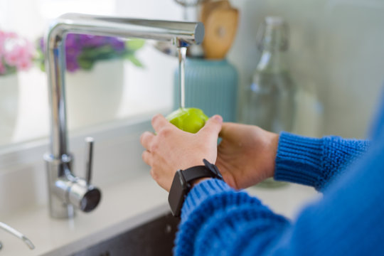 Young woman washing vegetables and fruit using water from sink