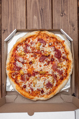 Italian pizza in cardboard box on wooden table. Top view