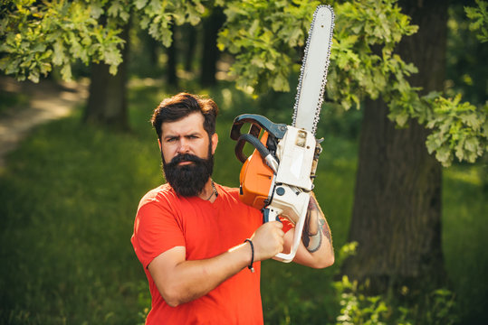 Lumberjack worker standing in the forest with chainsaw. Chainsaw. Stylish young man posing like lumberjack. Woodcutter with chainsaw on sawmill. Harvest of timber.