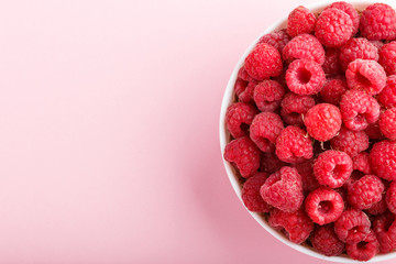 Fresh raspberry in white bowl on pink pastel background. top view.