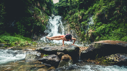 Young woman practice yoga near waterfall in forest