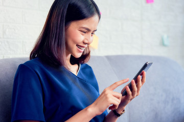 Happy young Asian woman using smartphone on the sofa in house.