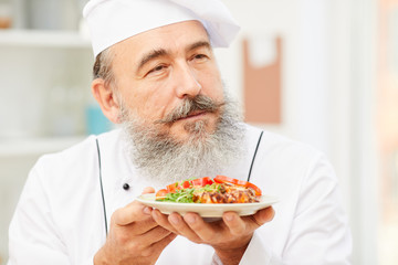 Portrait of blissful senior chef presenting meat steak while cooking in restaurant kitchen, copy space