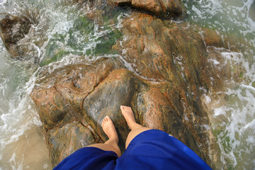 Legs stand on rock  covered with sea grass and waves