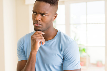 Handsome young african man thinking and questioning with pensive face, hand on chin wondering about...