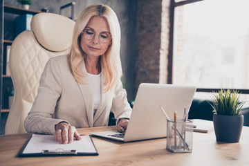 Low below angle view photo of blonde haired ceo analyzing income of her corporation by comparing information on laptop and writing clipboard