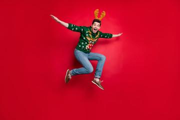 Fototapeta na wymiar Full length photo of funny jumping guy spread arms flying fast to sale x-mas shopping wear pullover with ugly ornament isolated red color background