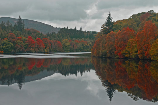 Beautiful view over Loch Faskally in Scottish Highlands with reflection of Autumn/Fall colors in trees. Landscape orientation.