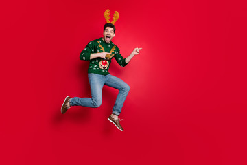 Fototapeta na wymiar Full size photo of funny jumping guy direct fingers empty space advising go sale prices shopping wear pullover with ugly ornament isolated red color background