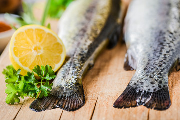Fresh rainbow trout tails with lemon and green leaves. Fishes on wooden board, selective focus.