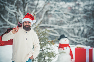 Christmas Man and snowman on white snow background. Snowman and funny bearded man in the snow. Hipster Santa Claus. Christmas and new year holidays.