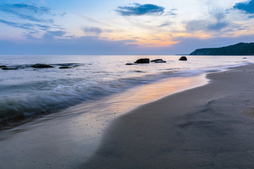 Obraz premium beautiful landscape of a wild sandy beach, a sea with protruding boulders on a long exposure and a steep coast on the horizon during sunrise