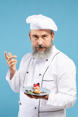 Waist up portrait of charismatic bearded chef presenting beautiful dessert while standing against blue background