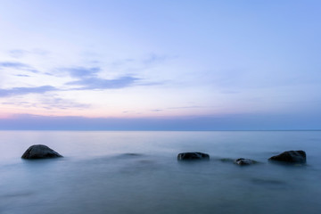 Fototapeta na wymiar long exposure smooth sea surface with large rocks sticking out of the water in twilight blue light
