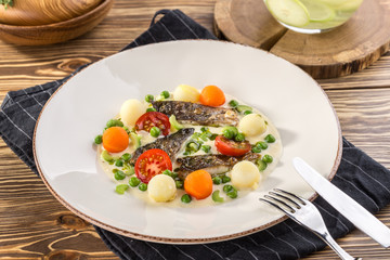 delicious portion of golden deep fried sea fish served on white plate with cooked carrots and potato on wooden table