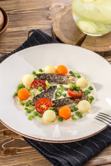 delicious portion of golden deep fried sea fish served on white plate with cooked carrots and potato on wooden table