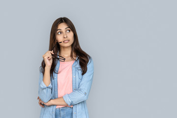 Curious young adult indian woman standing isolated on grey background with copy space. Dreaming...