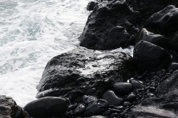 Volcanic stones on ocean shore, cold clean water, waves, Madeira island, Portugal