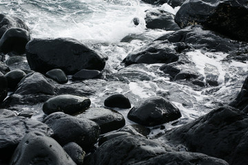 Volcanic stones on ocean shore, cold clean water, waves, Madeira island, Portugal
