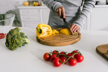 selective focus of woman cutting yellow paprika near cherry tomatoes and broccoli