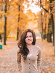 Brunette girl with long hair stands on the background of Golden autumn landscape, beautiful colorful trees