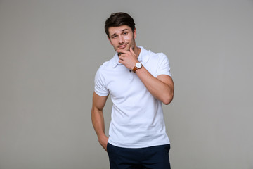 Image of young brunette man looking at camera and touching his chin