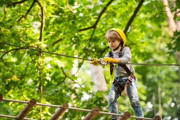 Naklejka na ściany i meble Little child climbing in adventure activity park with helmet and safety equipment. Happy little child climbing on a rope playground outdoor
