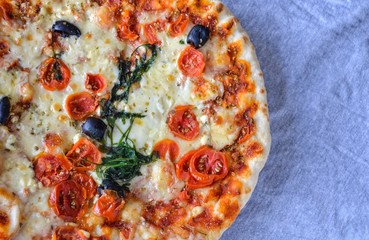 Half of delicious vegetarian pizza with cherry tomatoes, olives, arugula and cheese on gray background close up, top view