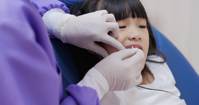 Little girl in a patient in a dental clinic. Dentist in an uniform and latex gloves is flossing her teeth with a help of a dental floss.