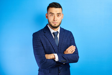 Portrait of serious handsome successful kazakh asian businessman in suit with arms crossed on blue studio background , isolated with copy space