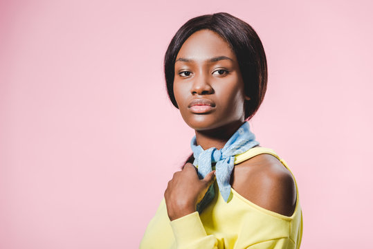 african american woman in yellow pullover and scarf looking at camera isolated on pink