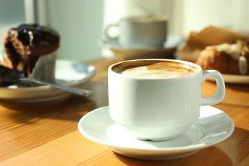 Cup of fresh aromatic coffee and cupcake at table in cafe