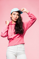 Naklejka premium attractive and pensive asian woman in pink pullover and cap looking away isolated on pink