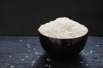 Milled rice in a black bowl on a black wooden floor in dark tone