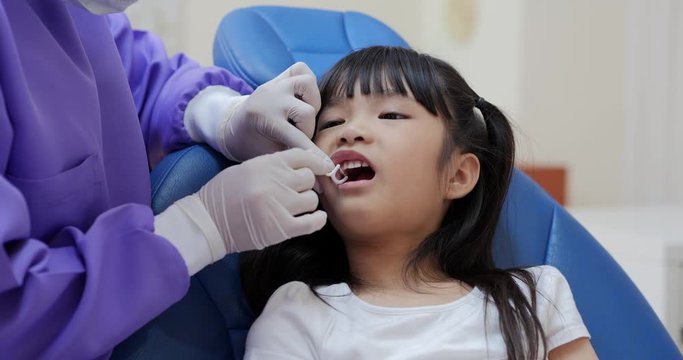 Little girl in a patient in a dental clinic. Dentist in an uniform and latex gloves is flossing her teeth with a help of a dental floss.