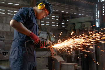 Diverse Asian male engineer operating power tools with sparks in industrial factory