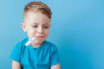 Ill young child with a thermomether, measuring the height of his fever and looking into the camera