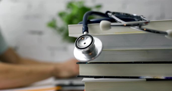 stack of books with stethoscope and medical student working on laptop