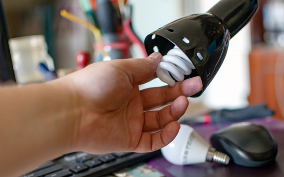 man's hand spins an energy-saving light bulb into a lamp on the desktop