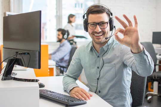 Happy handsome technical support operator with headset showing ok gesture to the camera