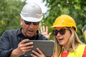 Work problem. Two scared, disappointed and surprised construction workers (male and female) reading bad news on the digital tablet